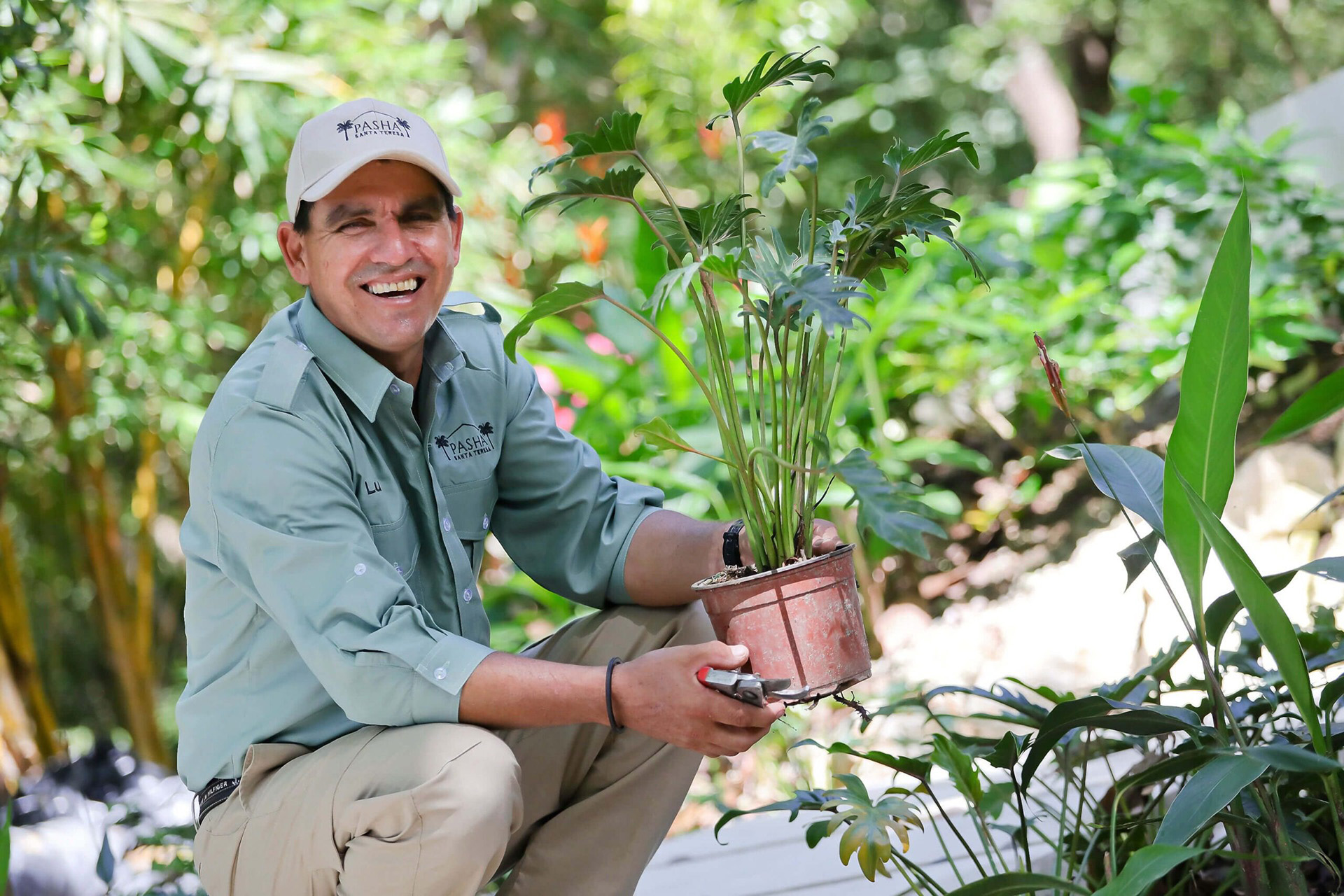 Gardener smiling at the camera, holding a green plant at Pasha Beachfront Estate